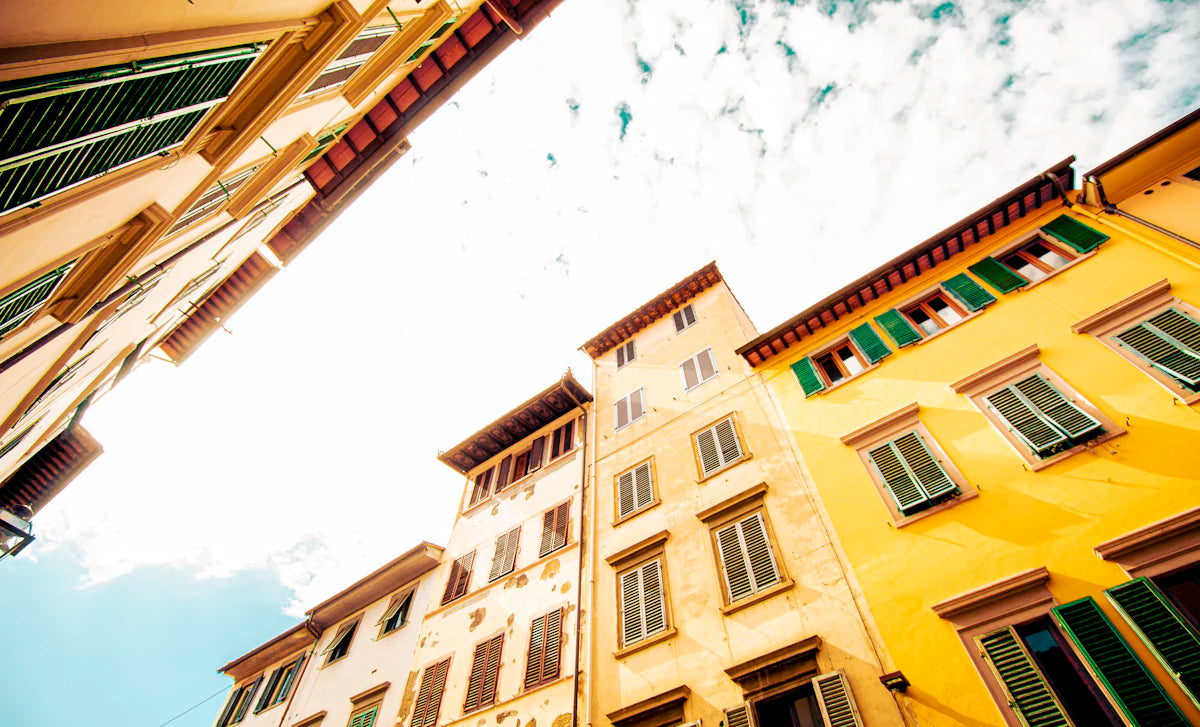 Warm yellow buildings and green shutters seen from a street in Florence